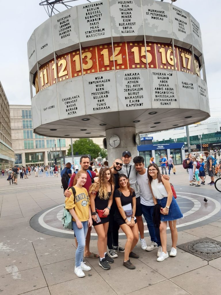Jugendliche posieren lachend vor der Weltzeituhr auf dem Berliner Alexanderplatz.