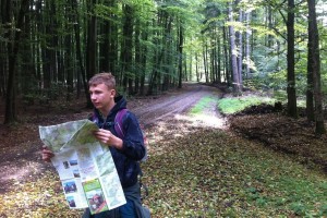 Ein Jugendlicher auf einem Waldweg. Er hält eine große Karte in der Hand, um sich in der Umgebung zu orientieren.