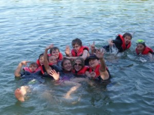 Eine Gruppe Kinder planschen im Wasser und lachen dabei in die Kamera