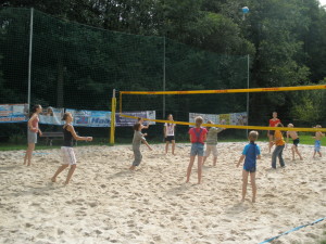 Eine Gruppe Jugendlicher auf einem Beachvolleyballfeld wie sie gerade gegeneinander spielen.
