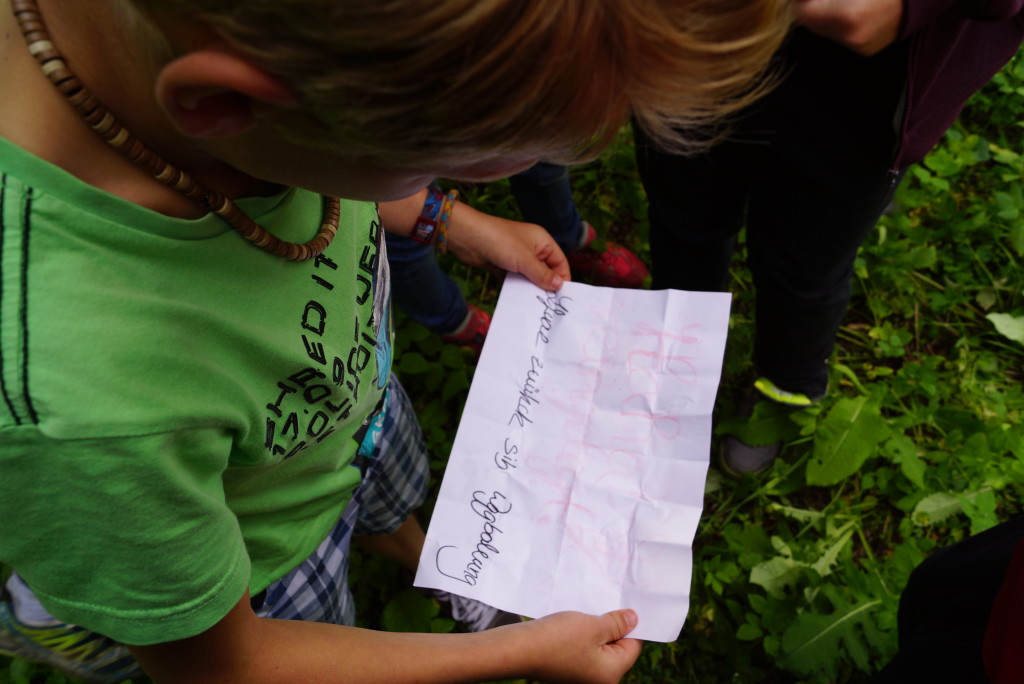 Ein Junge wird von schräg oben gezeigt, wie er einen Zettel mit einem Rätsel in der Hand hält und das Rätsel liest.