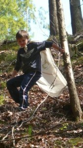 Ein Junge mit weißem Umhang geht einen steilen Abhang im Wald hinunter und hält sich zur Stabilisation an einem Baum fest.