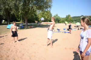 Mehrere Jugendliche spielen am Sandstrand Beachvolleyball.
