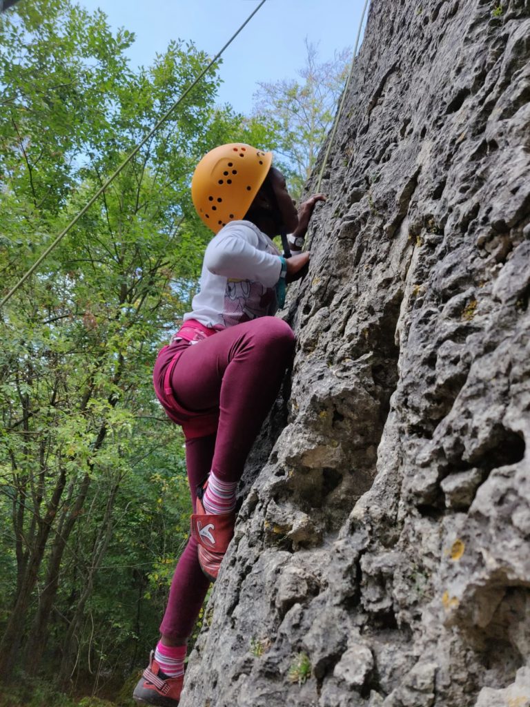 Ein Mädchen mit Helm klettert gesichert einen Felsen hoch.